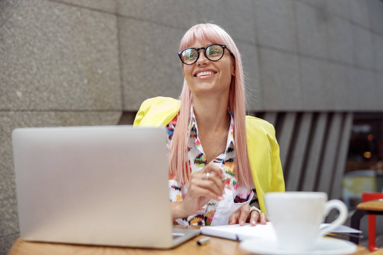 Mulher com o cabelo rosado sorrindo com um blazer amarelo