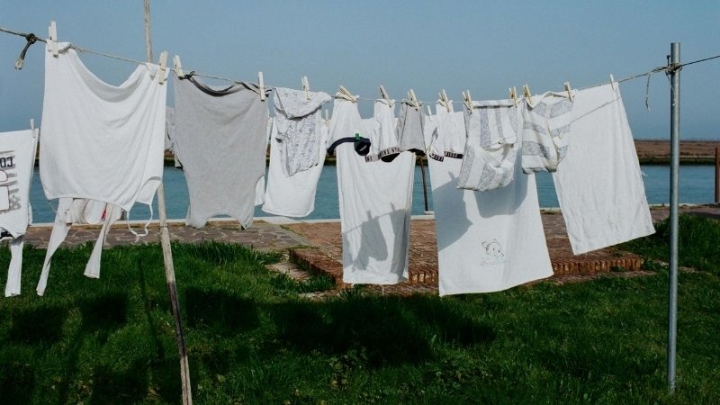 Roupas brancas estendidas em um varal sob o sol, representando o processo de secagem natural que ajuda na prática de como tirar mancha amarela de roupa branca e preservar o brilho dos tecidos.