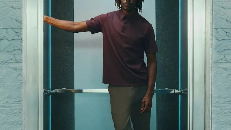 Homem com camisa polo vinho em look casual sofisticado dentro de ambiente moderno.