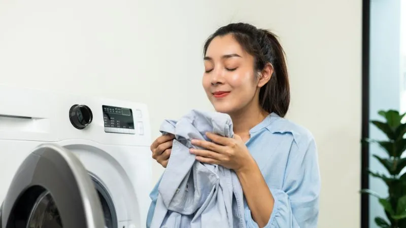 mulher cheirando roupa perto de maquina de lavar