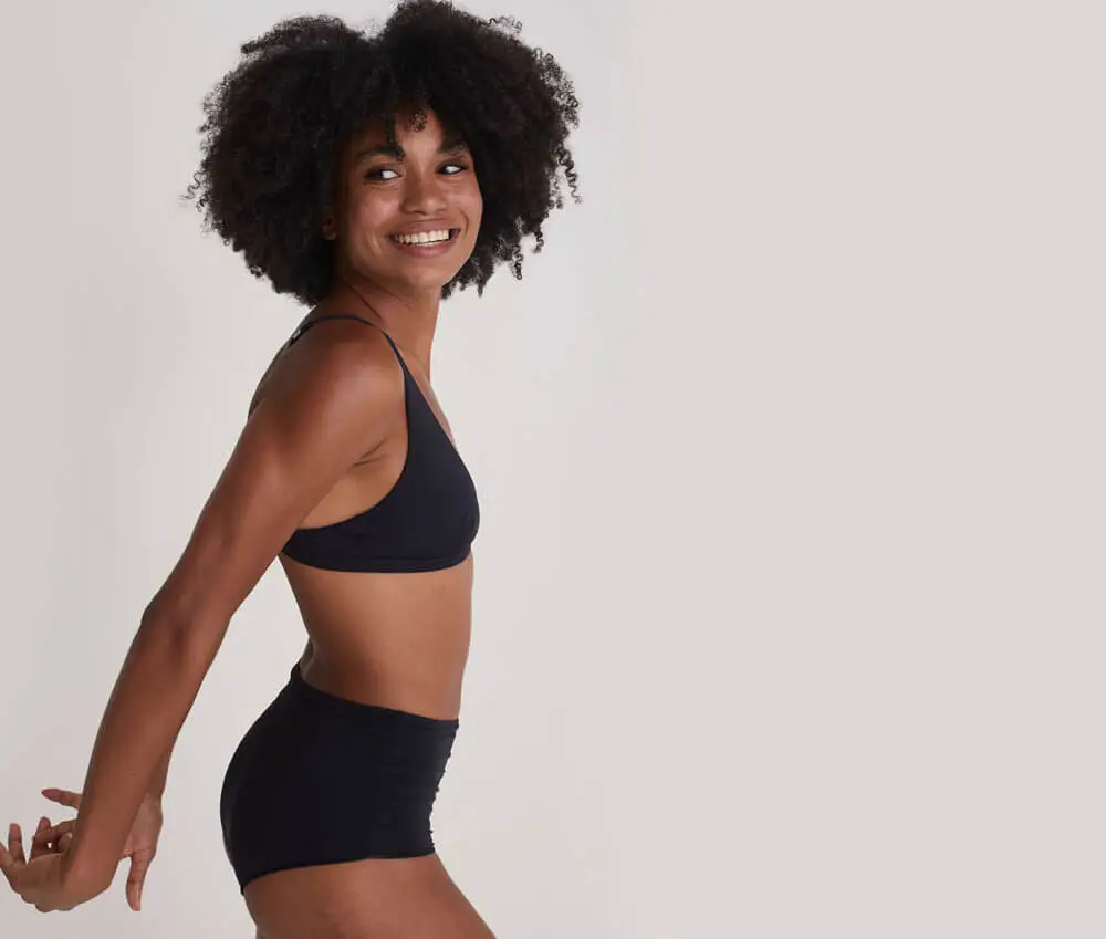 Foto de uma mulher sorrindo, com o corpo de lado e os braços estendidos para trás. Ela usa um tamanho de sutiã mais largo e alças fina, o modelo Flex da Insider.