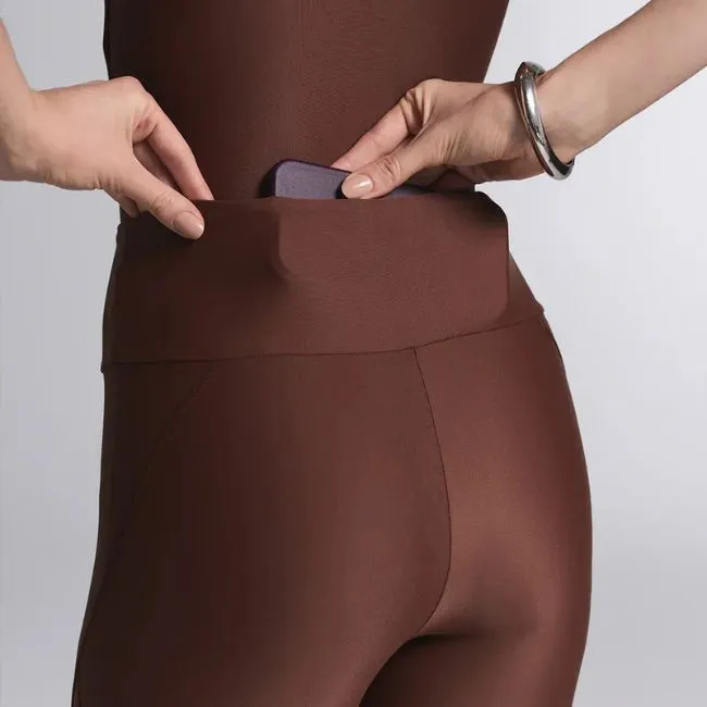 Detalhe de bolso funcional em legging marrom de academia, tecido tecnológico com elasticidade e ajuste ao corpo.